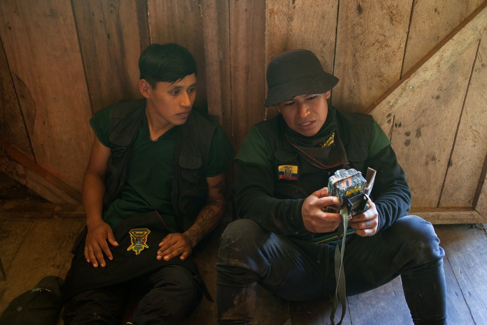 Marcelo Lucitante, a member of the Cofan indigenous guard, shows a fellow guard member footage from a camera trap used to record the passage of trespassing illegal gold miners, in Sinangoe, Ecuador, on April 21, 2022. Thomson Reuters Foundation/Fabio Cuttica