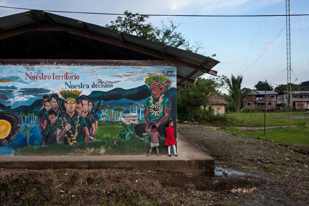 Children stand near a painted mural with the slogan, "Our territory, our decision” at the Cofan village of Sinangoe in Ecuador’s northern rainforest, on April 21, 2022. In February, the Cofan celebrated a rare victory when Ecuador's constitutional court ratified a ruling that had suspended 52 formal gold mining concessions on their lands. Thomson Reuters Foundation/Fabio Cuttica